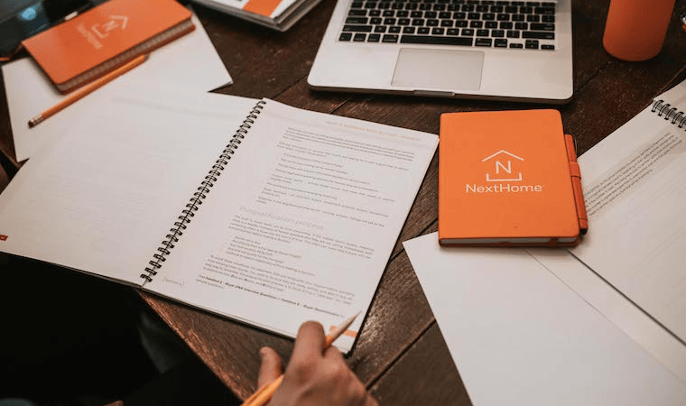 Notebooks branded with the NextHome Logo and a laptop on a wood desk